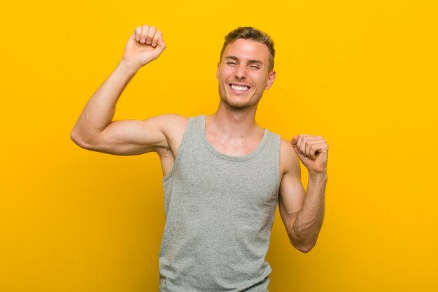 Jeune homme de sport caucasien célébrant une journée spéciale, saute et lève les bras avec énergie.