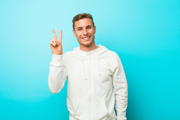 Jeune homme de sport caucasien joyeux et insouciant montrant un symbole de paix avec les doigts.