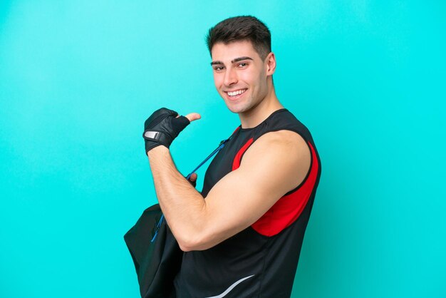 Jeune homme de sport caucasien avec sac de sport isolé sur fond bleu fier et satisfait de lui-même