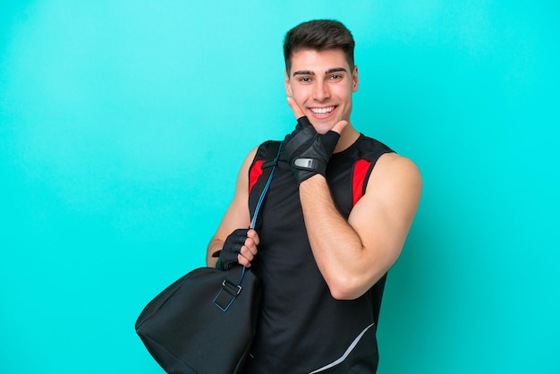 Jeune homme de sport caucasien avec sac de sport isolé sur fond bleu heureux et souriant