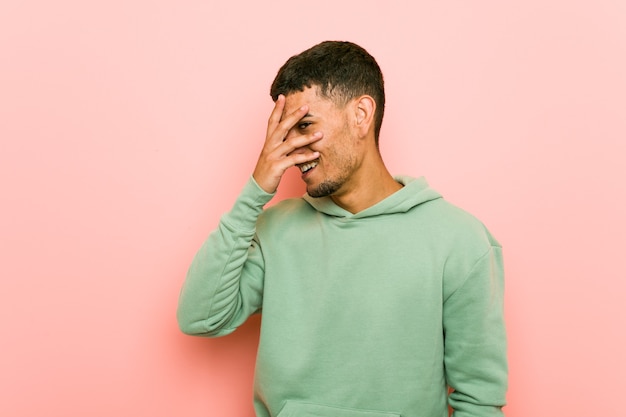 Jeune homme de sport hispanique cligner des yeux à la caméra à travers les doigts, visage couvrant embarrassé.