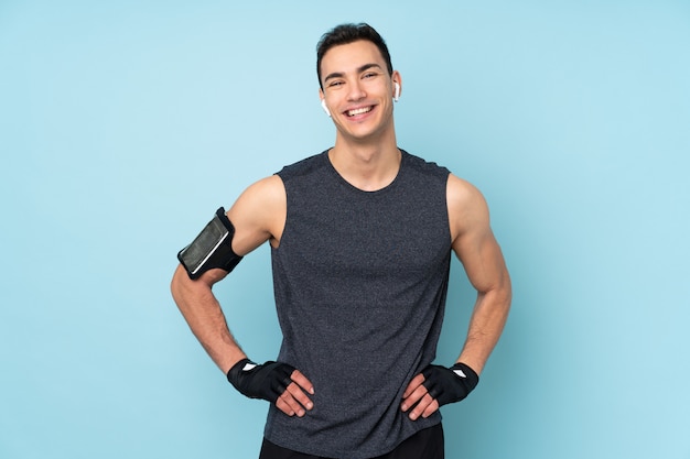 Jeune homme de sport sur mur bleu posant avec les bras à la hanche et souriant