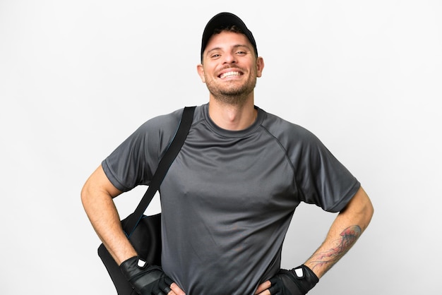 Jeune homme de sport avec sac de sport sur fond blanc isolé posant avec les bras à la hanche et souriant