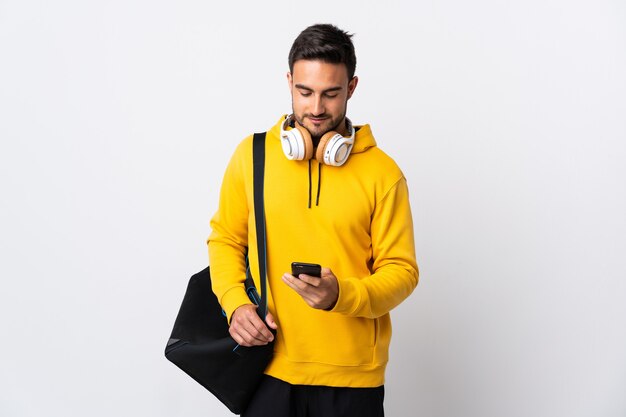 Jeune homme de sport avec sac de sport isolé sur blanc envoyant un message avec le mobile