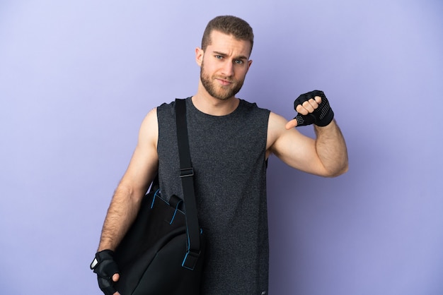 Jeune homme de sport avec sac de sport isolé sur blanc montrant le pouce vers le bas avec une expression négative