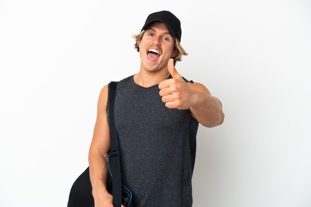 Jeune homme de sport avec sac de sport isolé sur fond blanc avec les pouces vers le haut parce que quelque chose de bien s'est passé