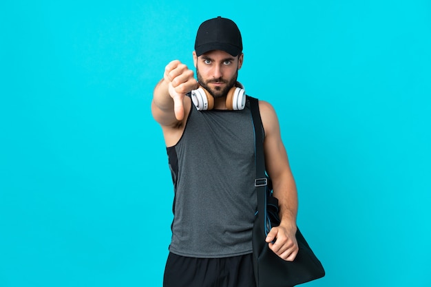 Jeune homme de sport avec sac de sport isolé sur fond bleu montrant le pouce vers le bas avec une expression négative