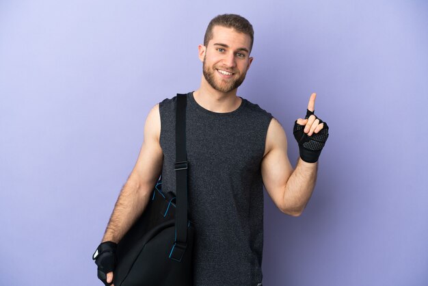 Jeune homme de sport avec sac de sport isolé sur un mur blanc montrant et en soulevant un doigt en signe du meilleur