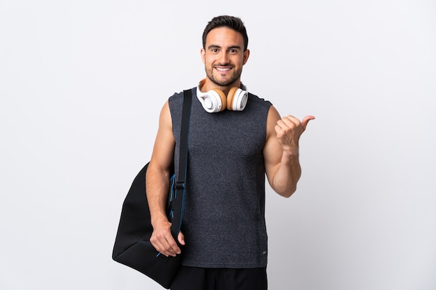 Jeune homme de sport avec sac de sport isolé sur un mur blanc pointant vers le côté pour présenter un produit