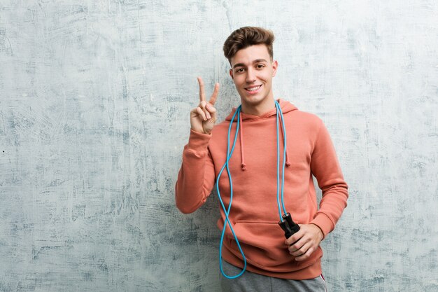 Jeune homme de sport tenant une corde à sauter montrant le numéro deux avec les doigts.