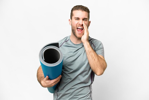 Jeune homme sportif allant à des cours de yoga tout en tenant un tapis sur fond blanc isolé criant avec la bouche grande ouverte