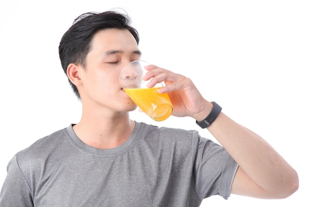 Jeune homme sportif asiatique beau et joyeux avec un verre de jus d'orange à la vitamine C isolé sur fond