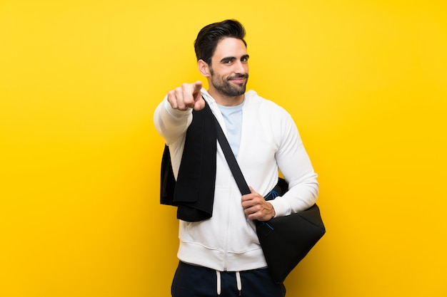 Jeune homme sportif au mur jaune isolé pointe le doigt vers vous avec une expression confiante