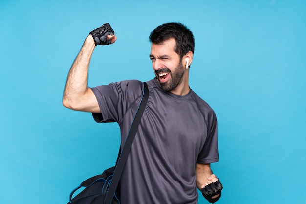 Jeune homme sportif avec barbe sur bleu isolé célébrant une victoire