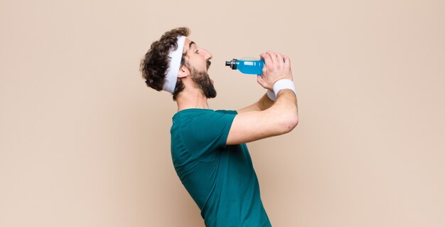 Jeune homme sportif avec une bouteille de boisson énergisante contre un mur plat