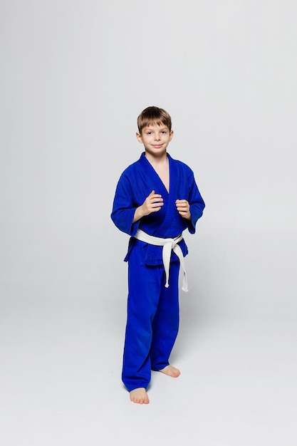 Jeune homme sportif en kimono bleu pour sambo judo posant sur fond blanc à la recherche de droite