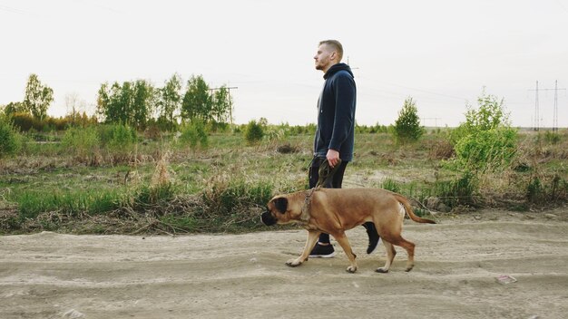 Jeune homme sportif marchant avec son chien bullmastiff en plein air dans la nature après une formation crossfit