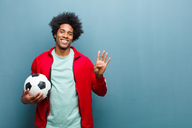 Jeune homme sportif noir avec un ballon de football contre wa bleu grunge