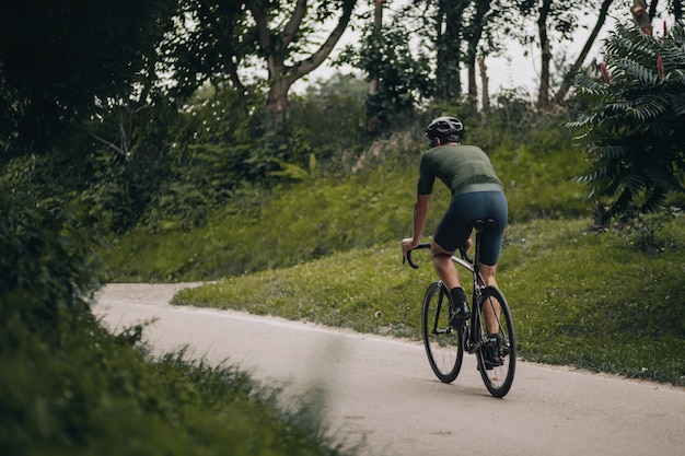 Jeune homme sportif portant un casque de protection faisant du vélo noir au parc de la ville verte. Homme actif profitant de son passe-temps préféré à l'air frais. Concept de modes de vie sains.