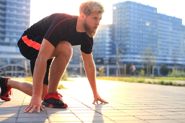 Jeune homme sportif en position de départ en plein air au coucher ou au lever du soleil