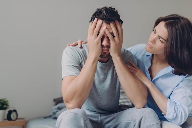 Un jeune homme stressant pleure de désespoir une mère aimante essaie de le calmer pose ensemble au lit contre l'intérieur domestique a quelques problèmes Le mari bouleversé ne voit aucune issue dans une situation difficile