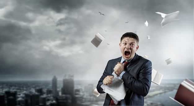Jeune homme stressé fou au travail, déchirant des documents avec une expression faciale frustrée. Technique mixte