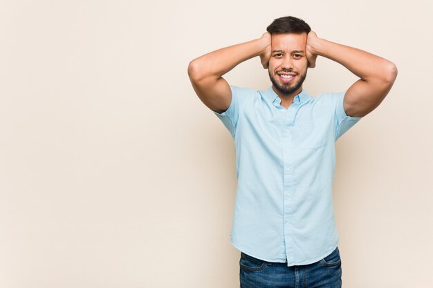 Jeune homme sud-asiatique rit joyeusement en gardant les mains sur la tête