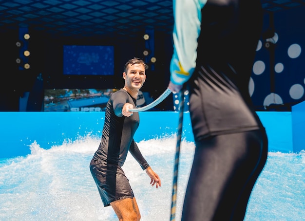 Un jeune homme surfe avec un entraîneur sur un simulateur de vagues dans un parc d'attractions aquatiques