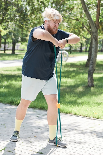 Jeune homme en surpoids faisant de l'exercice avec une corde de sport pendant l'entraînement sportif dans le parc