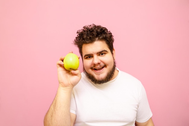 Jeune homme en surpoids positif isolé sur fond rose avec pomme verte à la main