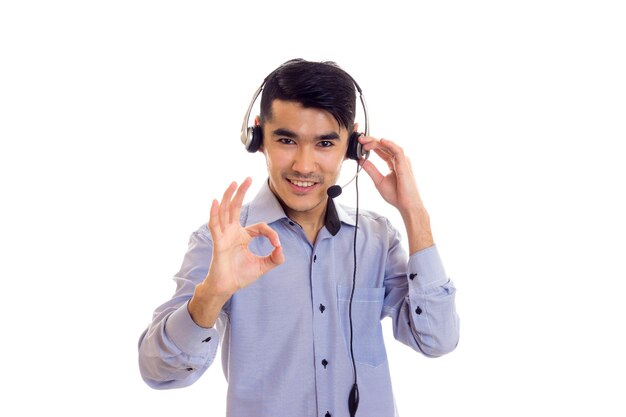 Jeune homme sympa aux cheveux noirs en chemise bleue avec un casque noir montrant bien en studio