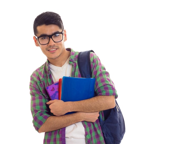 Jeune homme sympa aux cheveux noirs en T-shirt blanc et chemise à carreaux avec sac à dos bleu tenant des livres