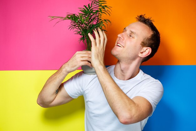 Jeune homme en T-shirt blanc, arrière-plan coloré, palmier décoratif, photo d'émotions, plante à la maison, amour de la nature