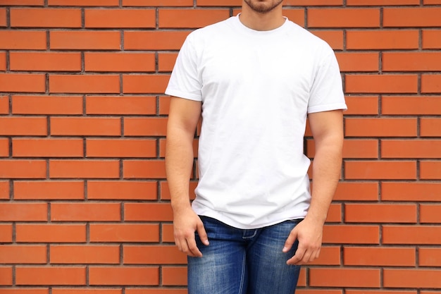 Jeune homme en t-shirt blanc debout contre le mur de briques agrandi