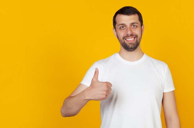 Jeune homme en t-shirt blanc montrant le pouce vers le haut avec un sourire heureux