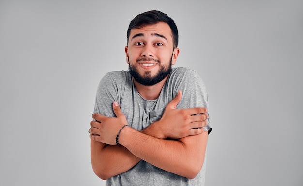 Un jeune homme en T-shirt gris se figea en se serrant dans ses bras. Fond gris studio.