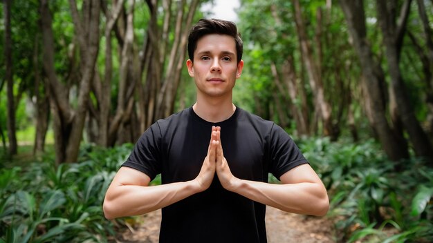 Photo un jeune homme en t-shirt noir montrant un geste de namaste et regardant avec espoir la vue de devant