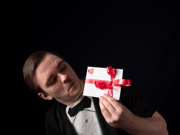 Photo un jeune homme en t-shirt noir montre avec surprise une carte postale blanche sur fond noir