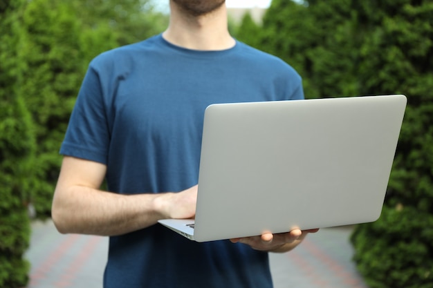 Jeune homme en t-shirt tenant un ordinateur portable en plein air