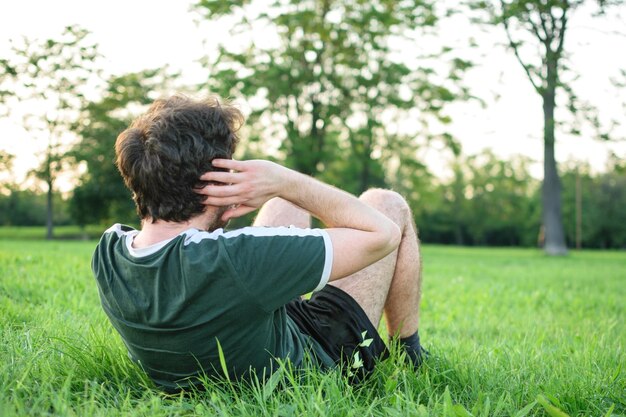 Jeune homme avec un t-shirt vert faisant des redressements assis dans le parc