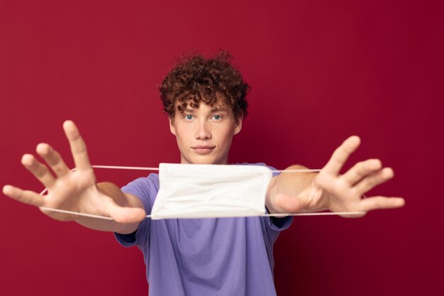 Un jeune homme en t-shirts violets masque médical dans les mains sécurité fond rouge inchangé