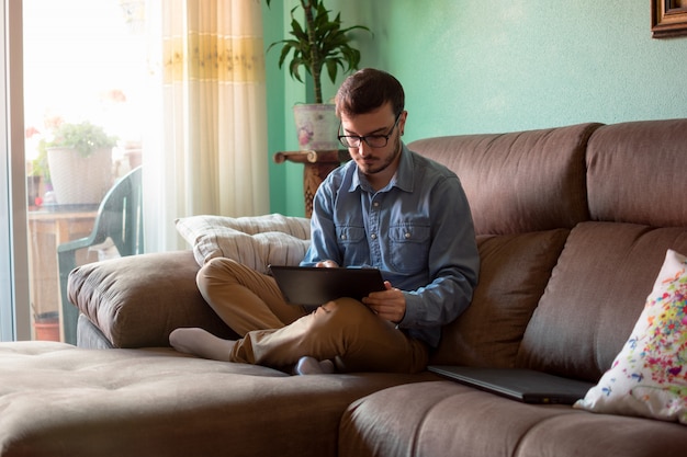 Jeune homme avec tablette sur canapé à la maison