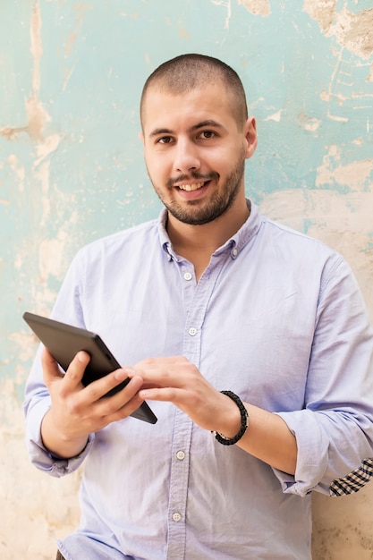 Jeune homme avec tablette par le mur