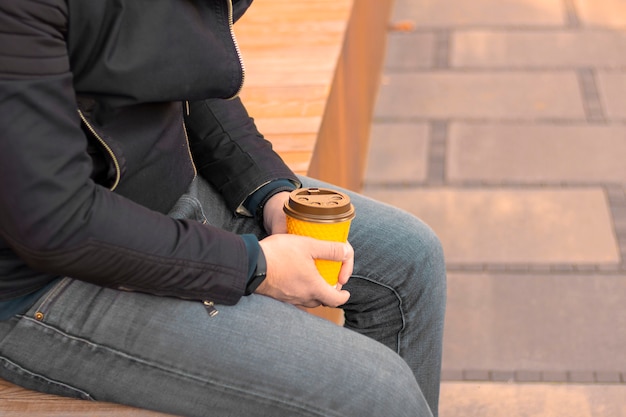 un jeune homme avec une tasse de café dans les mains est assis dans la rue main tenant une tasse de café en papier