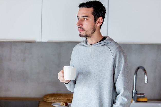 Jeune homme avec une tasse de café restant à la cuisine à la maison. Portrait candide