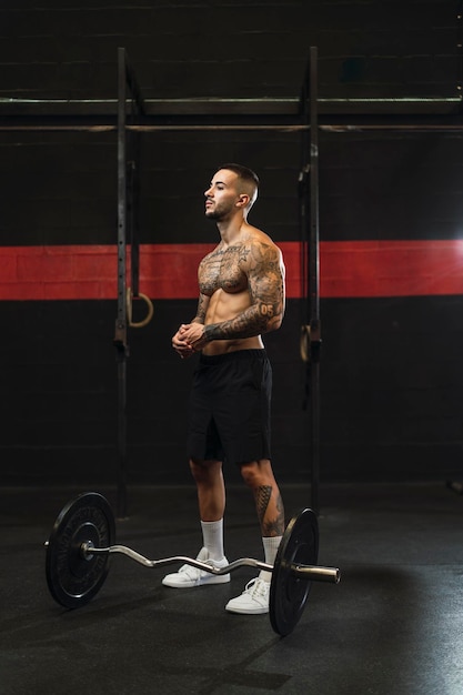 jeune homme tatoué faisant du sport dans une salle de sport avec des poids et un rameur