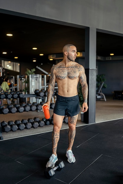 Un jeune homme tatoué avec un physique en forme pose dans une salle de sport