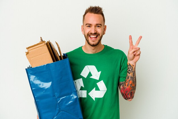 Jeune homme tatoué de race blanche en carton recyclé isolé sur fond blanc joyeux et insouciant montrant un symbole de paix avec les doigts.