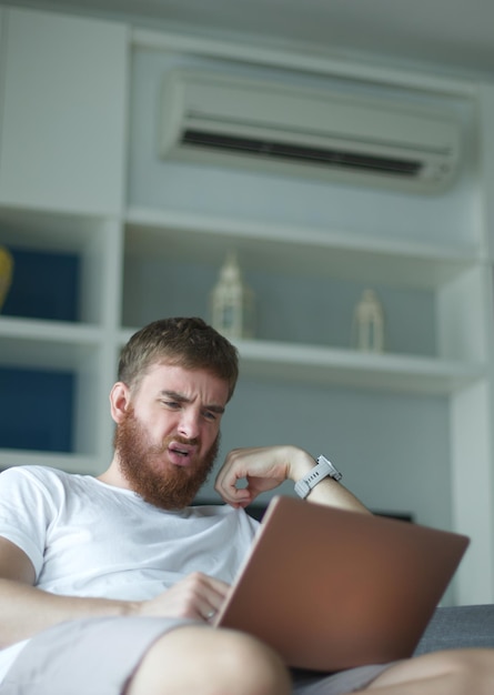 Jeune homme avec télécommande de climatiseur utilisant le climatiseur à la maison, le gars se rafraîchit