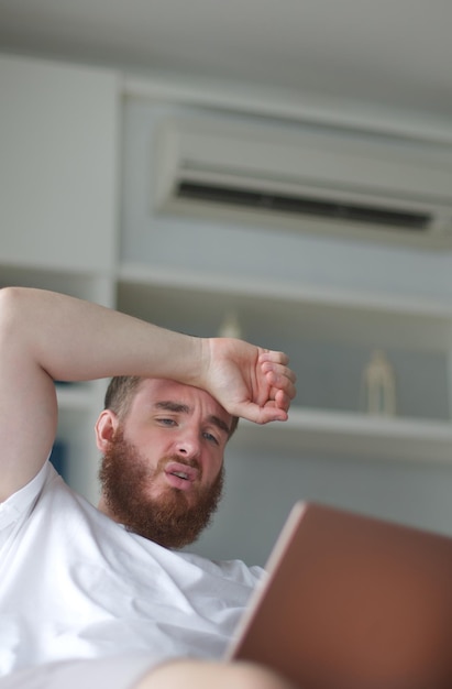 Jeune homme avec télécommande de climatiseur utilisant le climatiseur à la maison, le gars se rafraîchit